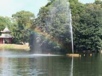 a fountain causing a rainbow on a pond